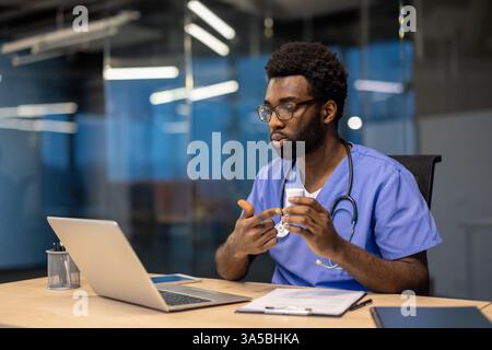 An African American doctor in scrubs explaining the medication uses during a telehealth appointment in his office, using a laptop. Stock Photo