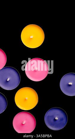 Tea lights in pink, yellow, and blue, top view composition against a black backdrop. Stock Photo