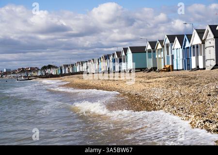 view of row of beach huts lined along Southend-on-sea beach front on sunny spring day, water waves breaking on cobbled beach Essex England UK Stock Photo