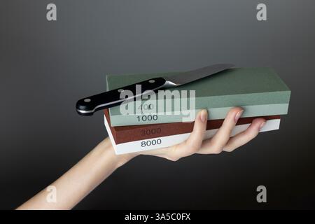 on a dark gray and wight background in a woman's hand there are sharpening stones of different colors and abrasiveness, gradation of hardness, small Stock Photo