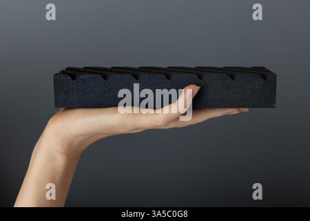 closeup on a dark gray background on a woman s palm lies a large abrasive grooved stone on top for sharpening knives and blades, an old method Stock Photo
