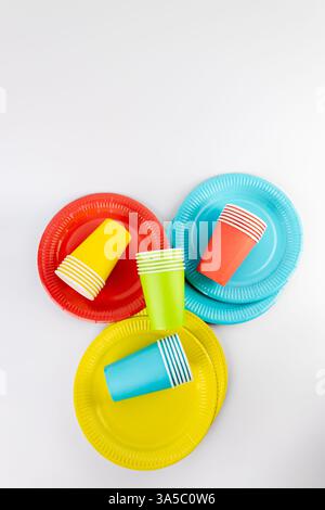 top shot on white background there are three paper cups yellow red and blue with matching paper plates set disposable tableware standard picnic set Stock Photo