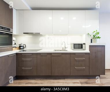 Modern kitchen featuring dark wooden cabinets, clean white countertop, essential appliances, and stylish decor. A cozy, functional, and contemporary s Stock Photo