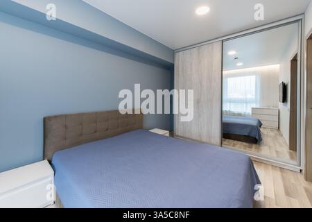 Bright bedroom interior featuring a modern design, with a cozy bed, television, and natural light through translucent curtains. A peaceful and minimal Stock Photo