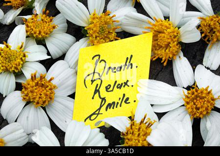 Breathe, Relax, Smile – Handwritten Motivation. Inspirational Message on Yellow Note with White Flowers Background Stock Photo