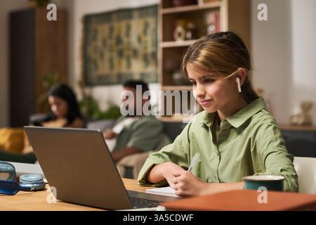 Group of employees in modern office space while woman in foreground with green shirt works on laptop and uses earphones for communication without distraction Stock Photo