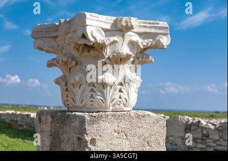 White marble corinthian capital featuring intricate acanthus leaf carvings, positioned on stone base at Kourion archaeological site near blue sky back Stock Photo