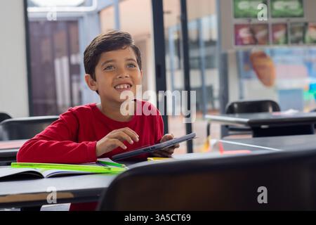 In school, smiling boy using tablet in classroom, engaging with technology, copy space Stock Photo