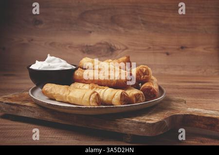 Fried spring rolls with cheese, on a wooden background, with cream sauce, no people Stock Photo