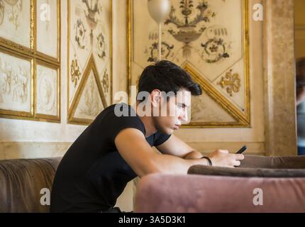 Young handsome man sitting in elegant cafeteria or restaurant using cell phone to send text message Stock Photo