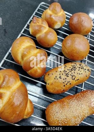 Various types of golden brown baked goods cool on a wire rack, showcasing different shapes and toppings in a cozy kitchen setting. Stock Photo