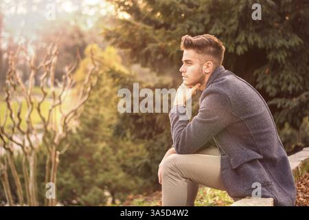 Handsome serious young man outdoors thinking, looking to the distance, pondering Stock Photo