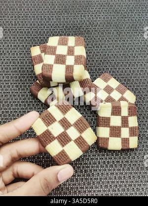 Colorful checkered cookies are artfully stacked on a dark textured ...