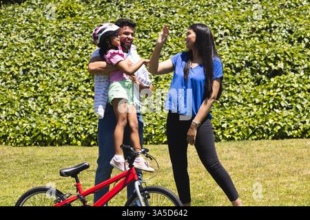 Family enjoying outdoor time, father lifting daughter, mother giving high five Stock Photo