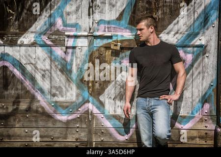 A man leaning against a wall with graffiti on it. Photo of a man leaning against a graffiti-covered wall Stock Photo