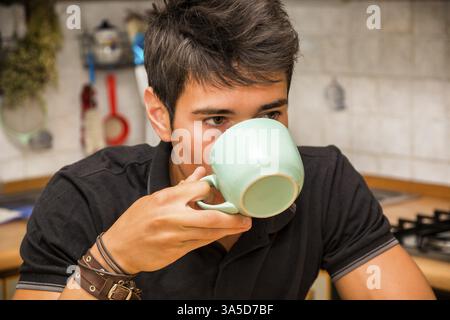 Attractive Young Man in Kitchen and Holding and Drinking from Cup of Coffee or Milk for Breakfast Stock Photo