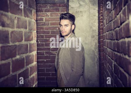 Attractive young man standing against brick wall, looking at camera Stock Photo