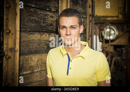 Handsome young man leaning against wood planks wall outdoor and looking at camera Stock Photo
