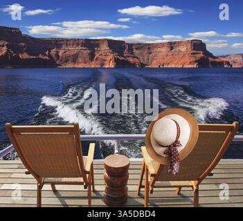 Waves from the boat cut through the Lake Powell. At the stern of the vessel are two deck chairs. On the back of one hanging elegant ladies straw hat Stock Photo
