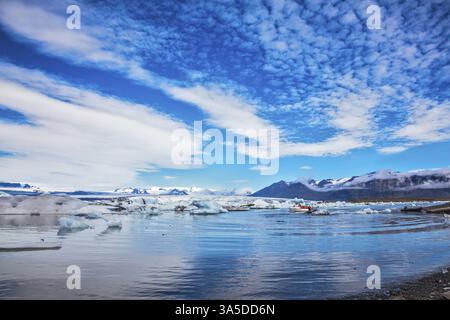 Magnificent summer morning in the ocean gulf with floating ice floes. The layered clouds fanning are reflected in a smooth surface of water. Ice lagoo Stock Photo