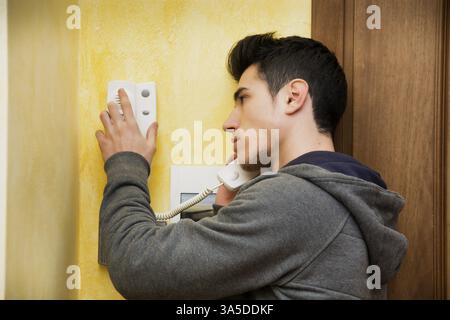 Teenager or young man answering the intercom in an apartment, pressing button to open entrance door Stock Photo