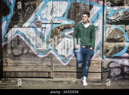 A man leaning against a wall with graffiti on it. Photo of a man leaning against a graffiti-covered wall Stock Photo