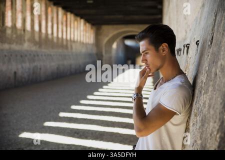 Handsome young man in old building against brick wall, looking down Stock Photo
