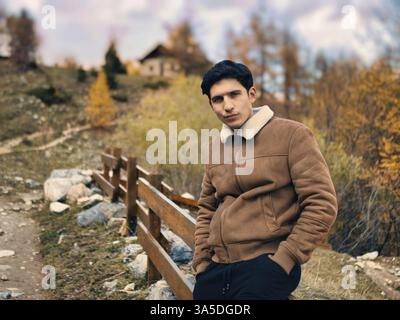 Attractive young man in the mountains in autumn or winter, cold weather, wearing suede jacket, looking at camera Stock Photo