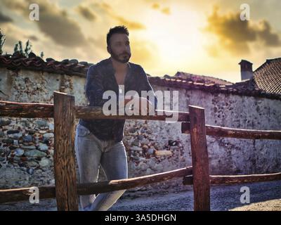 Handsome Hunky Young Man Outdoor in Countryside Leaning on Wood Fence, While Looking away Stock Photo