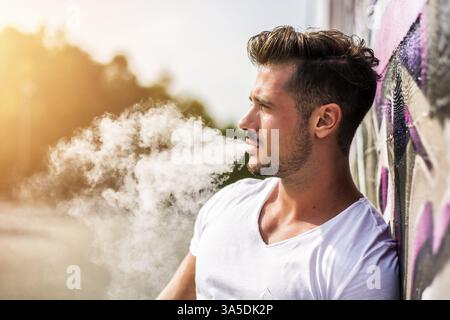 Attractive muscle man leaning on colorful graffiti wall, wearing white t-shirt Stock Photo