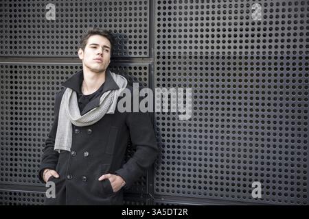 Serious Young Handsome Man in Winter Outfit Leaning on a Metal Wall While Looking to the Right of the Frame at Large Copyspace Stock Photo