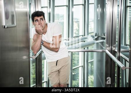 Scared young man desperate in stuck elevator screaming, looking very upset Stock Photo