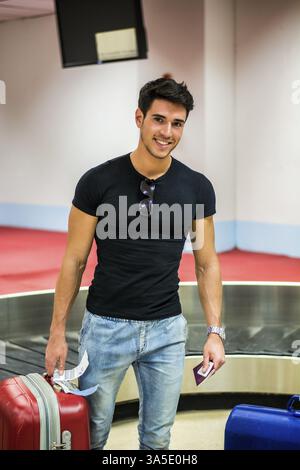 Cheerful young man standing in the airport with luggage Stock Photo