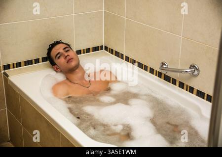 Handsome young man in bathtub at home having bath, looking at camera Stock Photo