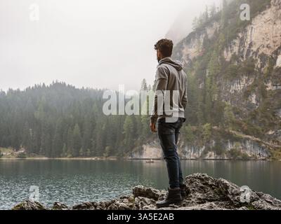 Handsome yung man standing on background of woods on shore of lake looking away Stock Photo