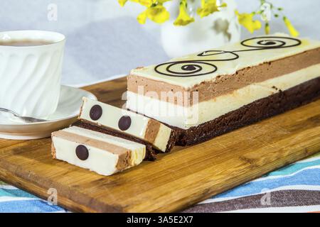 Three-layer chocolate cake, decorated with chocolate patterns. Background - white vase with flowers and porcelain cup with hot tea. Holiday cake Three Stock Photo