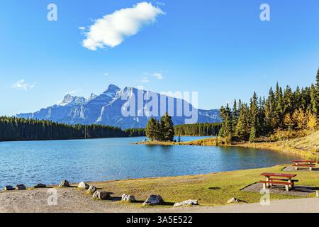 Picturesque area for outdoor recreation. Picnic table and benches. Rocky Mountains in Canada. The little island overgrown with evergreen spruce trees. Stock Photo