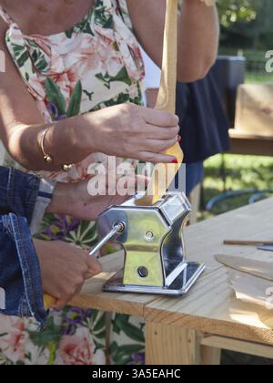 Hands of unrecognizable women preparing homemade pasta dough with a manual pasta rolling machine Stock Photo