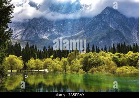 The sun's rays break through the clouds. The lake Fusine in Northern Italy. Mountains covered in mist. The smooth surface of the water reflects forest Stock Photo
