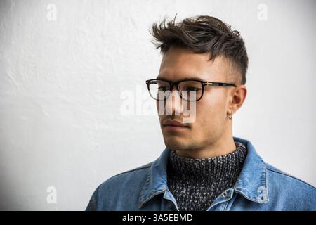 Handsome white asian young man wearing blue denim jacket, standing on light background against wall in studio shot Stock Photo