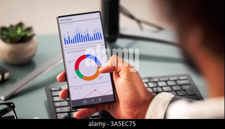 Smartphone In Hand, Young Black Man Predicts Business Market Performance Stock Photo