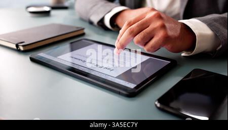 The young African American man is filling out a close-up online legal document using his tablet. He is carefully writing his last will and testament, Stock Photo