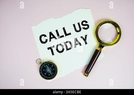 Call Us Today text written on paper with compass and magnifying glass flat lay on pink background Stock Photo