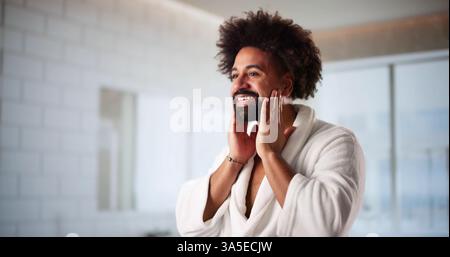American man with African skin applies facial cream in bathroom. Stock Photo