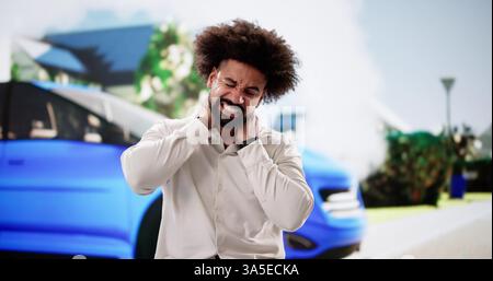 Man experiencing neck pain and stress after car accident near smoking vehicle. Insurance adjuster, auto mechanic, personal injury lawyer. Stock Photo