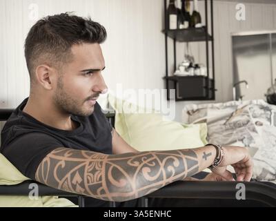 Handsome green eyed young man relaxing at home sitting on his couch, looking away to a side Stock Photo