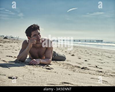 Handsome young man on beach in a sunny day, laying on sand, thinking Stock Photo