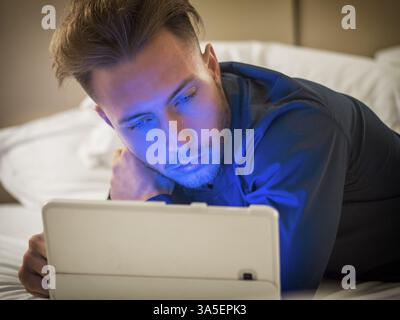 Handsome young man in bed typing on tablet PC, sending text message or dialing number or reading web pages Stock Photo