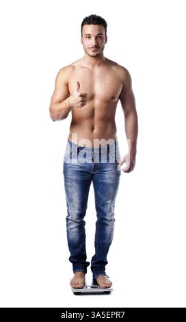 Muscular young man weighing himself on scale, making OK sign with thumb up Stock Photo