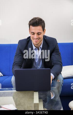 Attractive young man using laptop PC while laying on couch, with happy expression Stock Photo